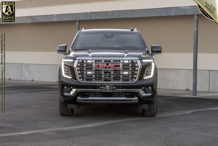 Front view of a black GMC Yukon SUV parked in front of a beige building with a metal roof overhang.