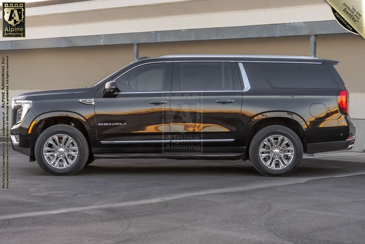 Side profile view of a black GMC Yukon Denali SUV parked in front of a beige building.